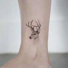 a small deer tattoo on the ankle is shown in black and grey ink, with an antelope's head behind it