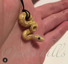 a hand holding a yellow and black snake necklace