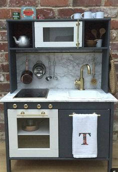 a toy kitchen with an oven, sink and stove top in front of a brick wall