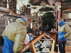 two men looking at books in a large room filled with bookshelves and people