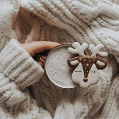 a person holding a mug with a reindeer brooch on it's side, while wearing a white sweater