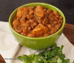 a green bowl filled with beans and parsley on top of a white napkin next to some cilantro