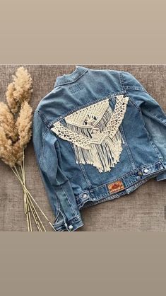 a denim jacket with an owl embroidered on the front and back, next to dried flowers