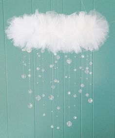 a white feather and beaded mobile hanging from the ceiling in front of a green wall