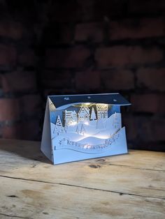 an origami box with a christmas scene on it sitting on top of a wooden table