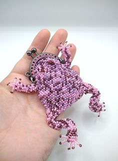 a hand holding a small purple beaded frog