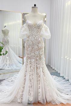 a white wedding dress on display in front of a mirror and mannequins