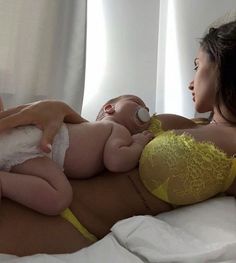 a woman laying on top of a bed next to a baby in a yellow bra