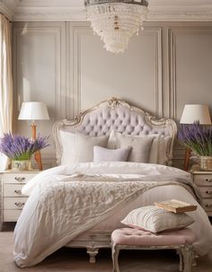 a white bed sitting under a chandelier next to two tables with lamps on them