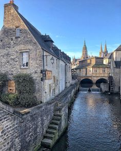 a river running between two buildings next to a bridge with a clock tower in the background