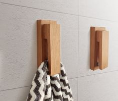 two wooden hooks on the wall with towels hanging from it's handles and one is holding a black and white towel