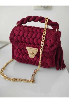 a red handbag sitting on top of a white table next to a gold chain