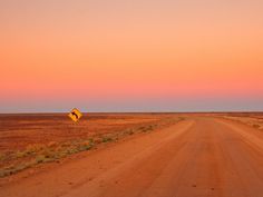 an empty dirt road with a yellow sign in the middle at sunset or sunrise time