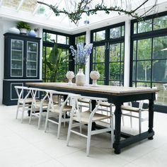 a dining room table with chairs and vases on it in front of large windows