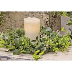 a white candle sitting on top of a wooden table next to green leaves and greenery