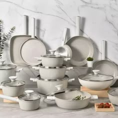 a table topped with lots of white pots and pans next to a wall covered in marble