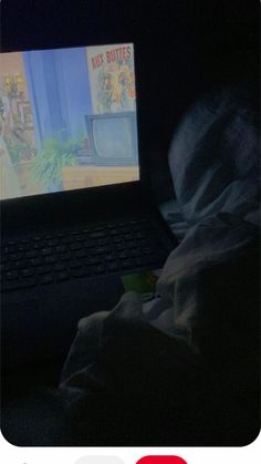 an open laptop computer sitting on top of a bed in the dark next to a blanket