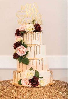 a three tiered cake with flowers and gold lettering on the top is sitting on a table