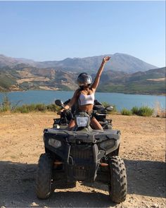 a woman riding on the back of an atv in front of a body of water