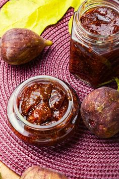 two jars filled with jam sitting on top of a pink place mat next to potatoes