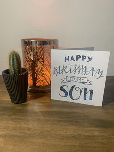 a happy birthday greeting card next to a cactus in a cup on a wooden table