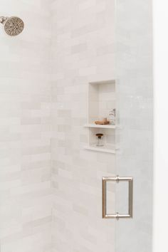 a white tiled shower with the door open and shelves on either side in front of it