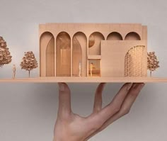 a hand is holding a model of a house on a shelf with trees in the background