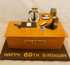 a birthday cake that is shaped like a desk with a man sitting at the top