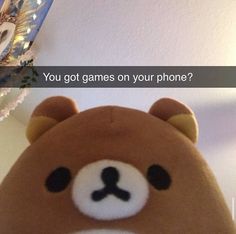 a brown teddy bear sitting on top of a table next to a plant and phone