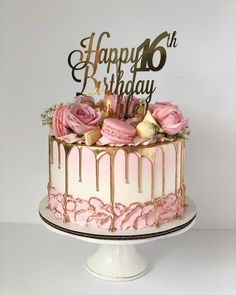 a birthday cake decorated with pink roses and gold drips on a white pedestal in front of a white background