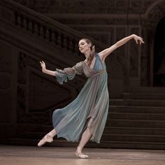 a woman in a blue dress is dancing on the dance floor with her arms stretched out