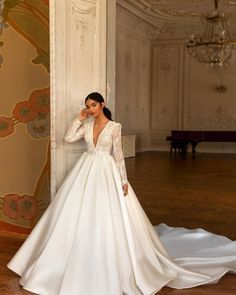 a woman in a long sleeved wedding dress leaning against a wall and talking on her cell phone