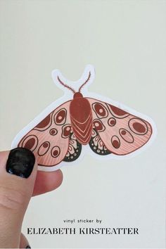 a hand holding a sticker with a moth on it