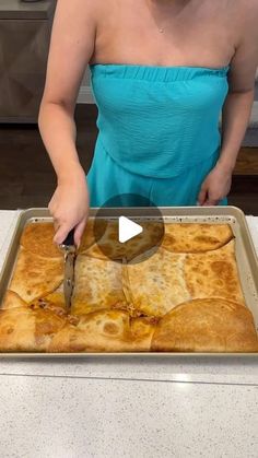 a woman in a blue dress cutting food on top of a sheet of baking paper