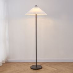 a floor lamp with a white shade on it in an empty room next to a window