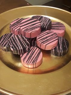 some pink and black cookies are on a gold platter with chocolates in the middle