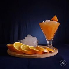 an orange drink with ice and lemon wedges on a wooden platter next to it