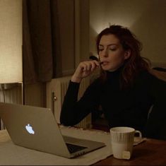 a woman sitting at a table with an apple laptop in front of her and looking at the screen