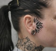 a woman with black tattoos on her neck and behind the ear is a rose tattoo