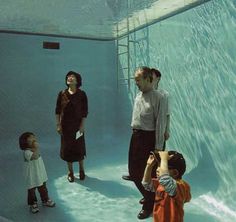 several people are standing in an aquarium looking at the water and one person is taking a photo