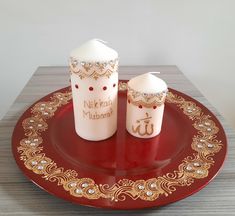 two small cups sitting on top of a red plate with gold trim around the edges