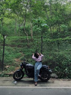 a woman sitting on top of a motorcycle in the middle of a forest with trees