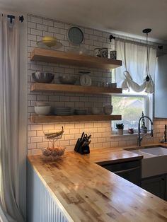 a kitchen with wooden counter tops and open shelving above the sink, next to a window