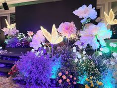 an arrangement of flowers is lit up in purple and blue lights at the end of a stage