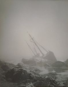 a boat that is sitting on some rocks in the ocean with foggy skies behind it