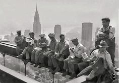 a group of men sitting on top of a building next to each other in front of a city skyline