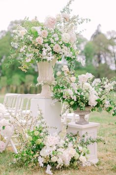 an arrangement of white flowers and greenery in vases on the ground at a wedding ceremony