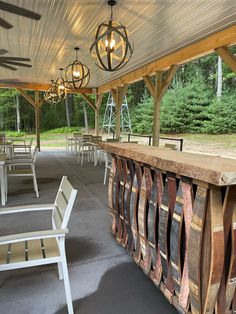 an outdoor bar made out of wine barrels with chairs around it and lights hanging from the ceiling