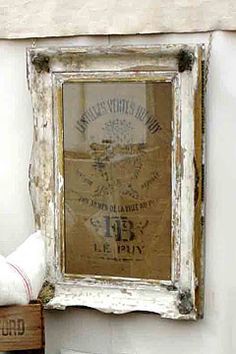 an old window frame is hung on the wall above a small wooden box and some books