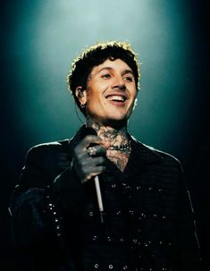 a man with tattoos on his chest holding a microphone and smiling at the camera while standing in front of a green light